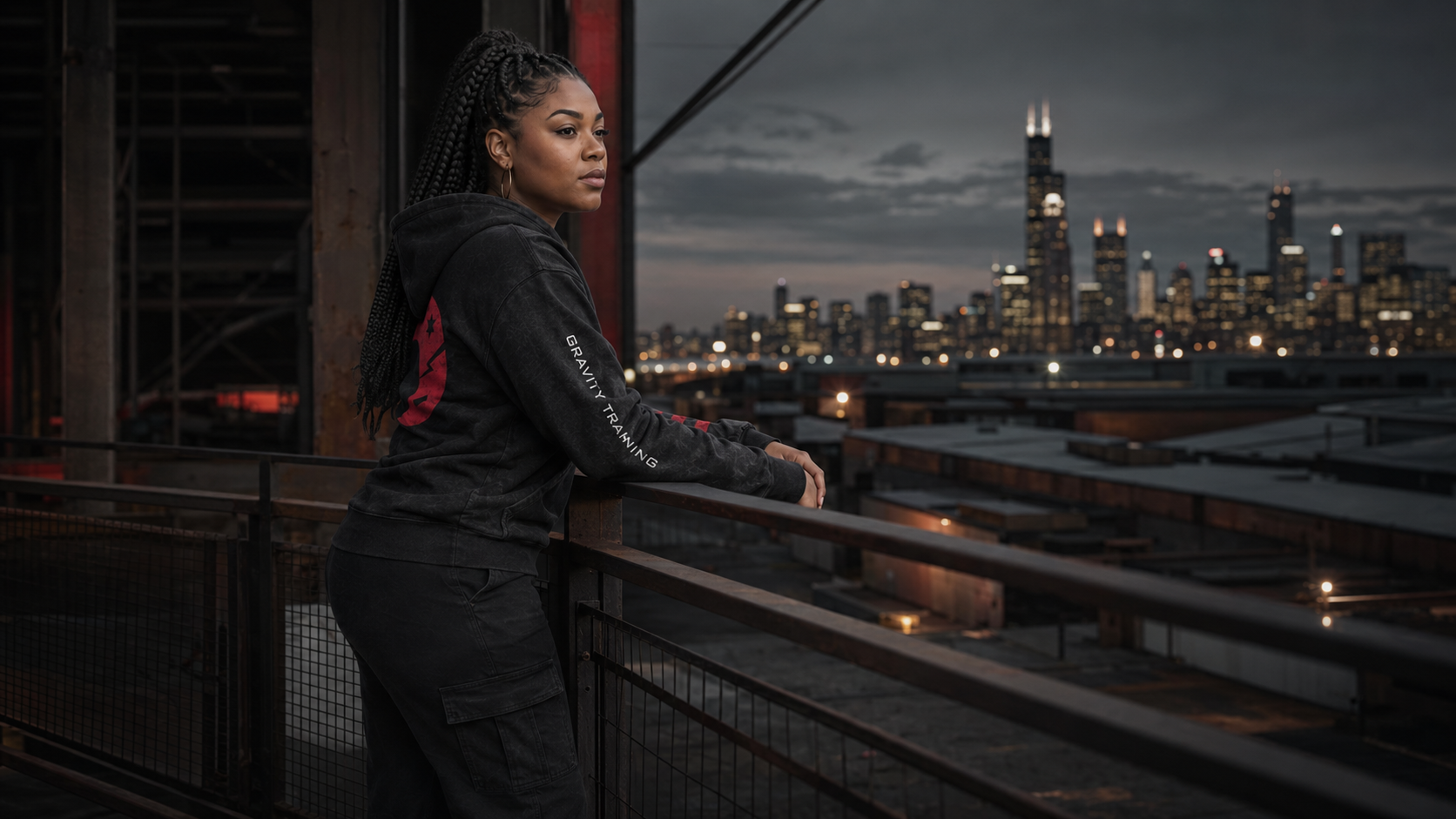 One adult woman in a fitted MMORBIT Gravity Training hoodie photographed in a moody warehouse campaign portrait